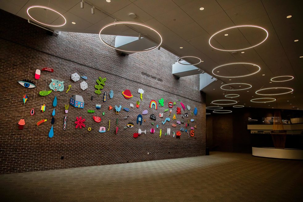 Brightly-colored paintings of various shapes are hung on a large wall of the Annenberg Center's lobby space.