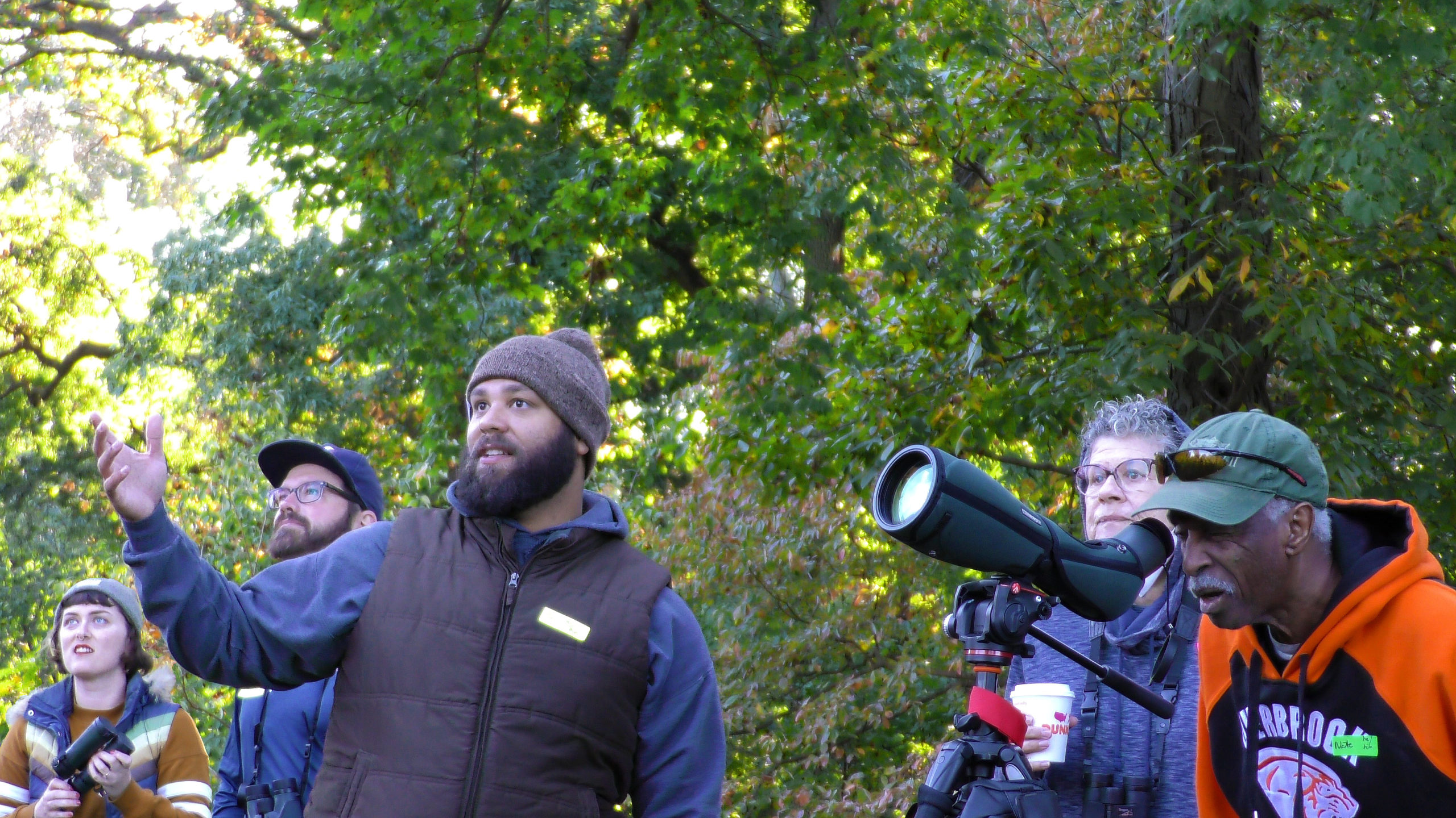 A group of people outside birding, looking at something outside of the left-hand side frame.