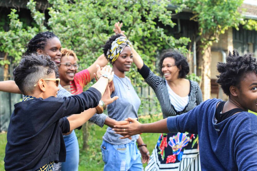Black women holding hands forming a circle and smiling.
