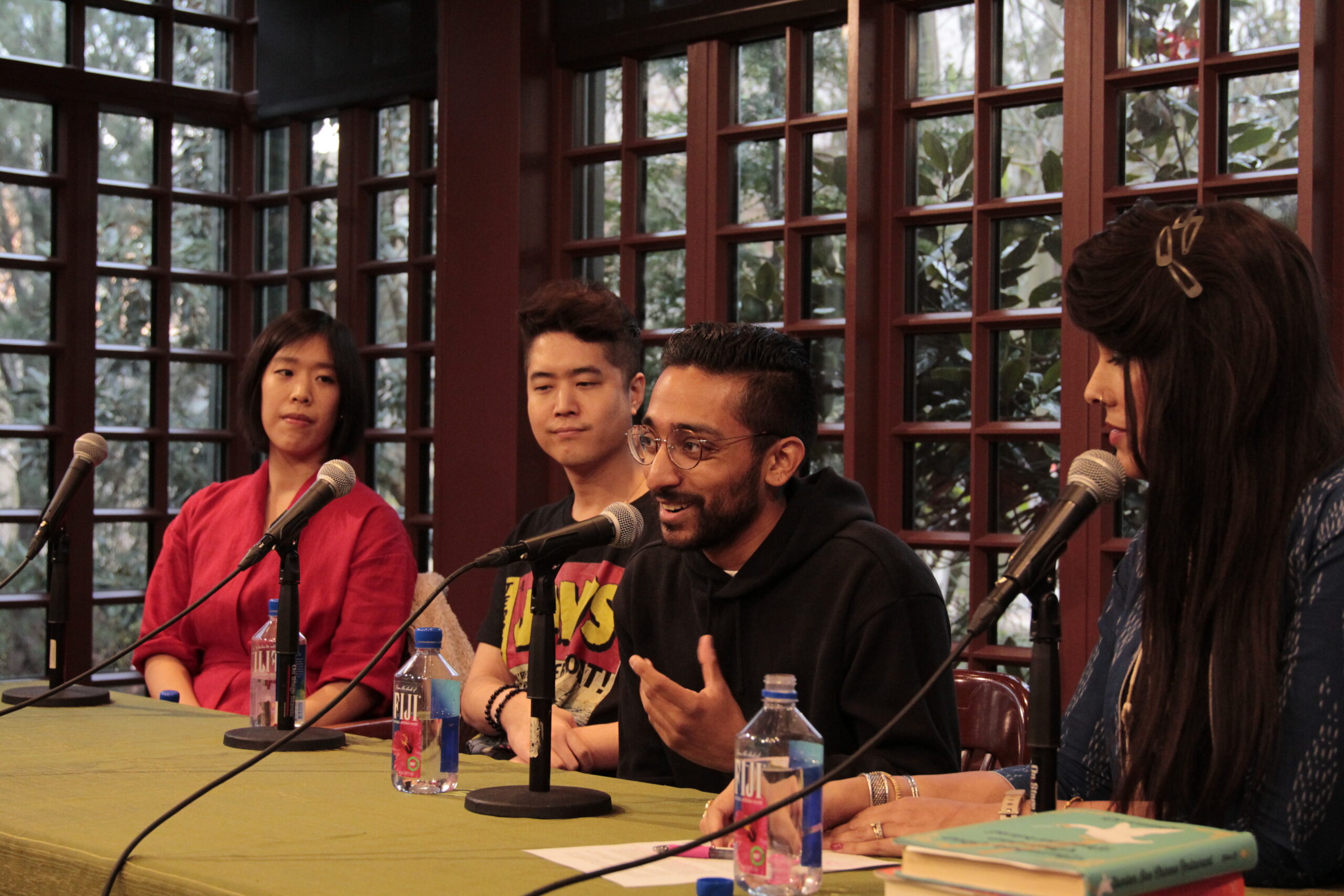 Four individuals sitting next to each other at a long table, with microphones in front of them, presenting for a panel discussion.