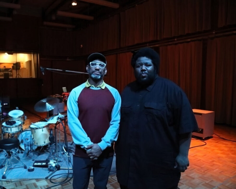 Musicians Tyshawn Sorey and King Britt standing in a recoding studio in front of a drum set.